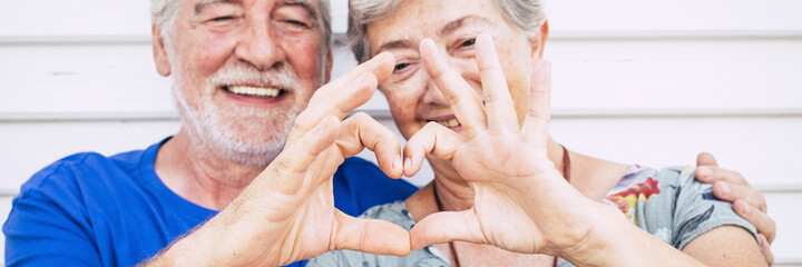 Senior people love hearth sigh with hands in banner header composition. Happy old man and woman smile in background