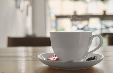Cоffee cappuccino in a white cup on a wooden table. Steam rises above the coffee. Selective focus on a cup in a cafe with background lighting