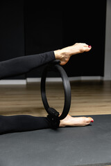 Slim legs of an athletic woman squeeze a pilates ring. Fitness with pilates magic circle in legs, workout in sportswear, gym