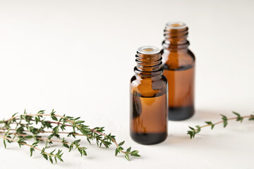 Thyme essential oil in a glass bottle close-up on a light background. Thyme branches are on the table.