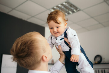 Little boy smiling cheerfully cute child redhead laughing baby playing with his father throws up son. Toddler having fun at home dressed overalls suspenders and white shirt. Happy childhood