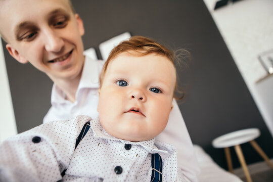 Little boy smiling cheerfully cute child redhead laughing baby playing with his father, son taking selfie video call. Toddler having fun dressed overalls suspenders and white shirt. Happy childhood
