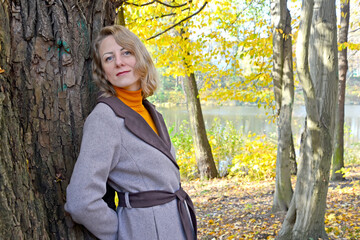The woman leaned against the trunk of an old tree by the lake. Autumn Park