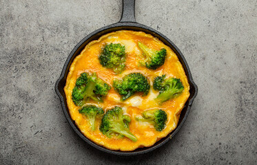 Healthy vegetarian egg omelette with green broccoli in black cast iron frying pan with fork and knife top view on gray stone concrete background table, diet and healthy clean eating concept 