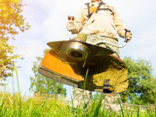 A male worker mows the grass with a gasoline trimmer. Bottom view, selective focus on the trimmer...
