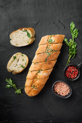 Baguette with parsley herbs butter, on black dark stone table background, top view flat lay