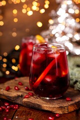 A glass of pomegranate cocktail with orange on the background of Christmas decorations and lights....