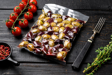 Olives in vacuum packaging for supermarket, on black wooden table background