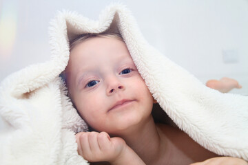 Cozy holidays at home. Cute little child lying under white knitted blanket and playing