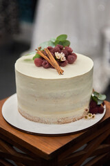 Elegant wedding or birthday cake decorated with fresh raspberries and cinnamon on table in...