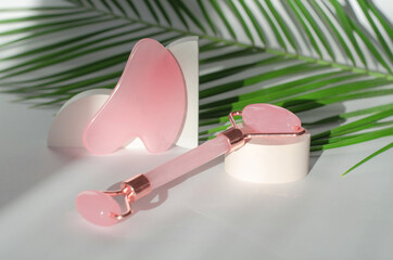 Roller jade facial massager on beige podium with shadows and palm leaf. Caring for the skin. Gua Sha Massager