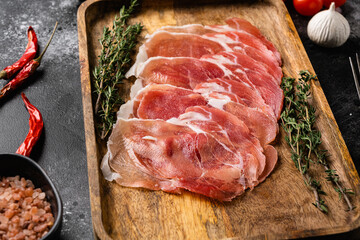 Appetizer from dry cured ham, prosciutto slices, on black dark stone table background