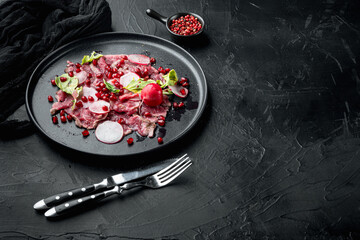 Carpaccio of marbled beef, with Radish and garnet, on plate, on black stone background, with copy...