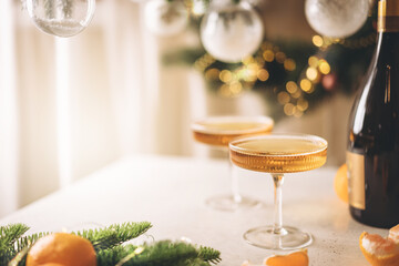 Two glasses of champagne and tangerines on a table against blurred christmas background with...