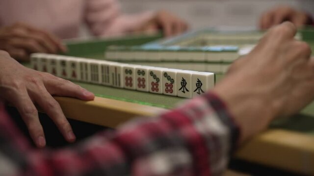 selective focus with closeup of mahjong tiles and the player's hand tapping on gambling table, planning scheme. chinese characters translation: east