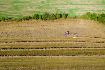 Aerial view on a tractor that collects hay in rows with a disc rake. Agribusiness concept