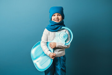 Kid boy with slad in hands. Winter sports and leisure concept childhood, studio shot on light blue background.