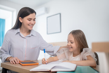 Fototapeta premium Joyful mother watching her daughter doing homework