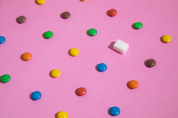 A pattern of sweets, colorful candies and one sugar cube. Pink background.
