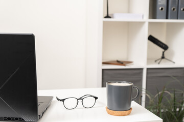 Close-up of a laptop, glasses and a cup of coffee on a white work table.