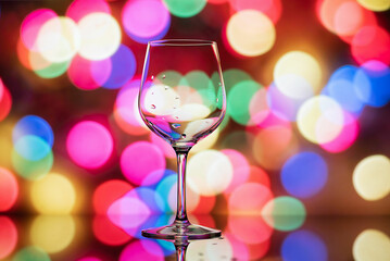 Transparent wine glass on a background of red-yellow, shiny bokeh. A wine glass on the background of Christmas lights. Wine glass shot in close-up