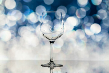 Transparent wine glass on a background of blue, shiny bokeh. A wine glass on a black and blue background. Wine glass shot in close-up