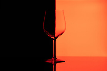 Transparent wine glass on a black and red background. A wine glass divided in half into black and red sides. A wine glass taken in close-up. Minimally photographed glass. Half of the glass is black, t
