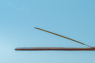 Minimalist close up of burning incense stick with smoke on a blue background