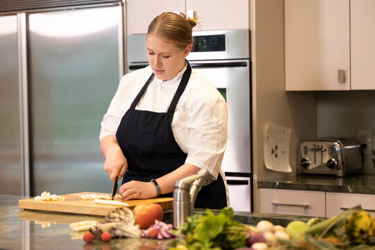 Professional Chef Megan Gill in kitchen looking down while cutting up vegetables.