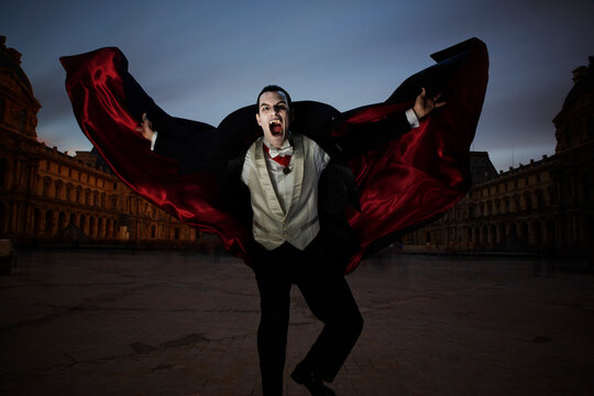 Count Dracula showing fangs and holding his cape out while running towards the camera at night