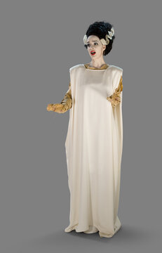 Full length portrait of a woman in a Bride of Frankenstein Halloween costume, making a horrified face, against a gray background
