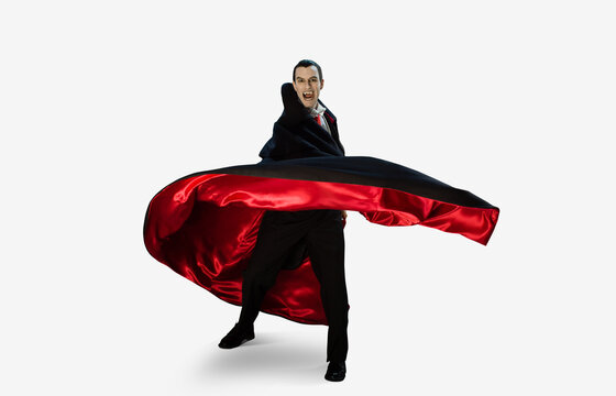 Portrait of a man dressed as a vampire against a white background quickly turning away from camera moving his cape with him