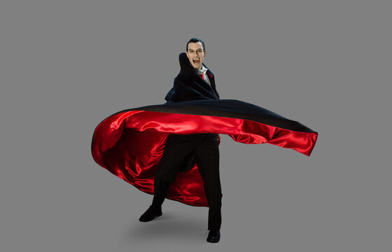 Portrait of a man dressed as a vampire against a gray background quickly turning away from camera moving his cape with him