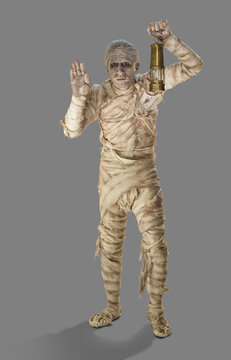 A mummy holding a lantern with one hand up looking into distance, against gray background 