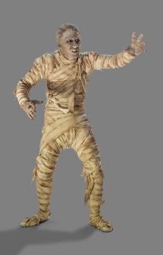 Full length portrait of a man dressed as a mummy wrapped in decaying bandages for Halloween making painful movements, against a gray background