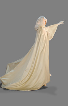 Portrait of a woman dressed as a ghost for Halloween turned profile with one arm reaching out , against a gray background