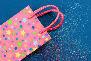 Pink gift bag on abstract red, white and blue glitter sparkle background. Holiday concept. Flat lay. Copy space.