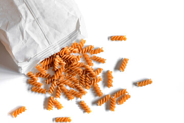 Whole grain eggless rye fusilli pasta on a white background spilled out of white paper bag