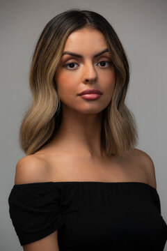 Portrait of Hispanic woman wearing off the shoulder top on gray background.