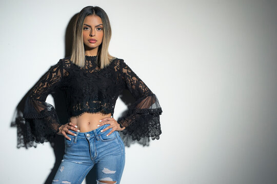 Young confident Hispanic girl with hands on hips leaning against white wall 