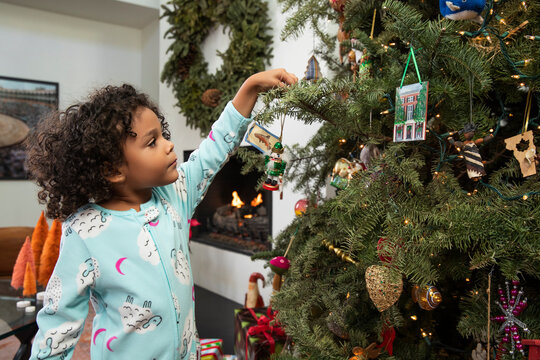 Child reaching up to hang an ornament on the lighted Christmas tree in her home