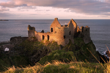 Dunluce Castle Sunset. The iconic ruins of Dunluce Castle perched on a rocky outcrop on the North Antrim Coast in Northern Ireland.
