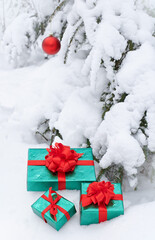 Gift boxes and a Christmas ball under the branches of a pine tree covered with snow in nature.
