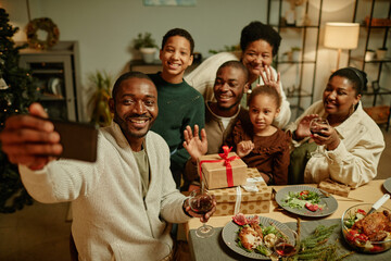 Fototapeta na wymiar High angle portrait of happy African-American family taking selfie photo while enjoying Christmas at home together