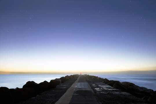 Looking down length of rocky breakwater leading out to the ocean in evening