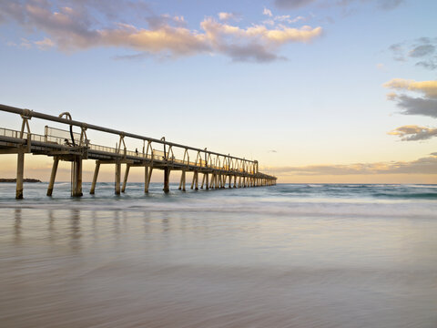 People walking and fishing on long jetty stretching out to sea in early evening