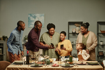 Portrait of big African-American family looking at smartphone screen while enjoying dinner party at...