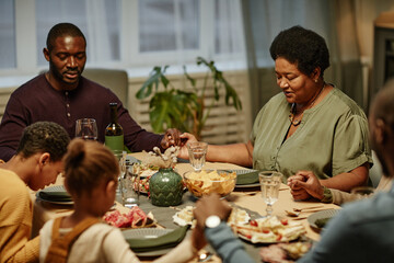 Portrait of African-American senior woman holding hands with family while saying grace during dinner party at home