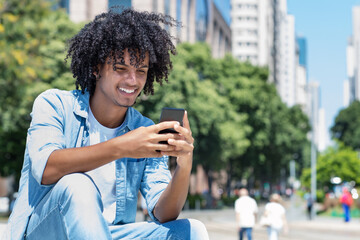 Latin american young adult man playing online game with mobile phone outdoor in city