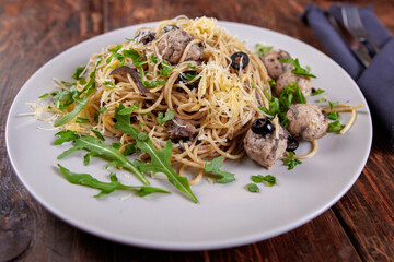 Spaghetti with meatballs, olives and arugula on wood table